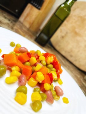 Beyaz tabakta parlak renkli sebzeler: mısır, bezelye, fasulye, biber, havuç, sağlığa iyi gelir, yemek pişirme