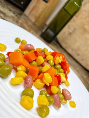 Beyaz tabakta parlak renkli sebzeler: mısır, bezelye, fasulye, biber, havuç, sağlığa iyi gelir, yemek pişirme