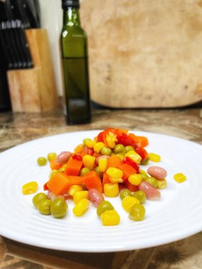 Beyaz tabakta parlak renkli sebzeler: mısır, bezelye, fasulye, biber, havuç, sağlığa iyi gelir, yemek pişirme