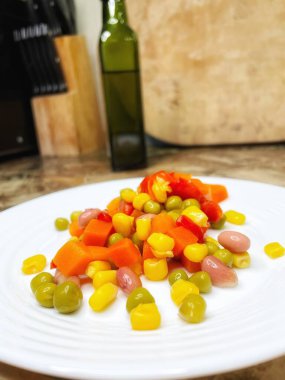 Beyaz tabakta parlak renkli sebzeler: mısır, bezelye, fasulye, biber, havuç, sağlığa iyi gelir, yemek pişirme