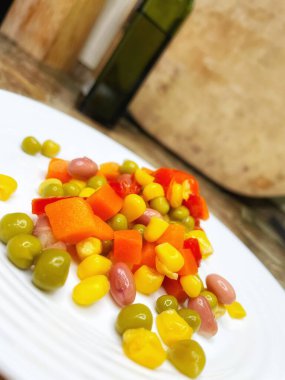 Beyaz tabakta parlak renkli sebzeler: mısır, bezelye, fasulye, biber, havuç, sağlığa iyi gelir, yemek pişirme