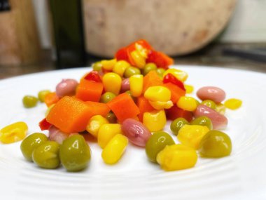 Beyaz tabakta parlak renkli sebzeler: mısır, bezelye, fasulye, biber, havuç, sağlığa iyi gelir, yemek pişirme