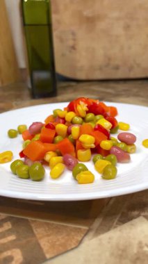 Beyaz tabakta parlak renkli sebzeler: mısır, bezelye, fasulye, biber, havuç, sağlığa iyi gelir, yemek pişirme