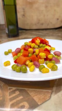 Beyaz tabakta parlak renkli sebzeler: mısır, bezelye, fasulye, biber, havuç, sağlığa iyi gelir, yemek pişirme