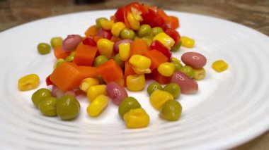 Beyaz tabakta parlak renkli sebzeler: mısır, bezelye, fasulye, biber, havuç, sağlığa iyi gelir, yemek pişirme