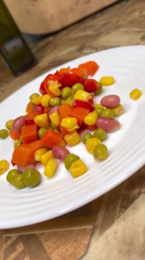 Beyaz tabakta parlak renkli sebzeler: mısır, bezelye, fasulye, biber, havuç, sağlığa iyi gelir, yemek pişirme