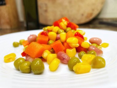 Beyaz tabakta parlak renkli sebzeler: mısır, bezelye, fasulye, biber, havuç, sağlığa iyi gelir, yemek pişirme