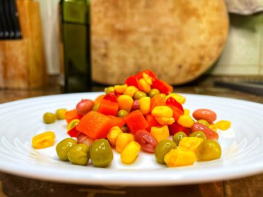 Beyaz tabakta parlak renkli sebzeler: mısır, bezelye, fasulye, biber, havuç, sağlığa iyi gelir, yemek pişirme