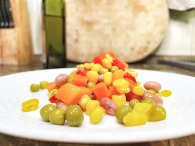 Beyaz tabakta parlak renkli sebzeler: mısır, bezelye, fasulye, biber, havuç, sağlığa iyi gelir, yemek pişirme