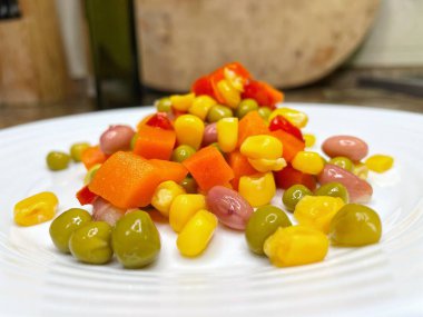 Beyaz tabakta parlak renkli sebzeler: mısır, bezelye, fasulye, biber, havuç, sağlığa iyi gelir, yemek pişirme