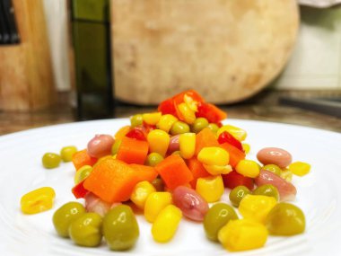 Beyaz tabakta parlak renkli sebzeler: mısır, bezelye, fasulye, biber, havuç, sağlığa iyi gelir, yemek pişirme