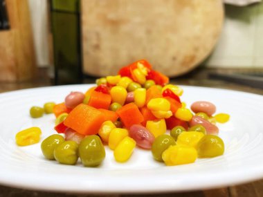 Beyaz tabakta parlak renkli sebzeler: mısır, bezelye, fasulye, biber, havuç, sağlığa iyi gelir, yemek pişirme