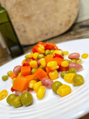 Beyaz tabakta parlak renkli sebzeler: mısır, bezelye, fasulye, biber, havuç, sağlığa iyi gelir, yemek pişirme