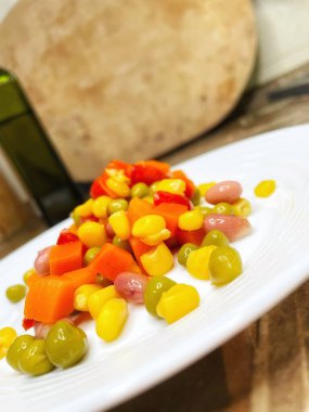 Beyaz tabakta parlak renkli sebzeler: mısır, bezelye, fasulye, biber, havuç, sağlığa iyi gelir, yemek pişirme