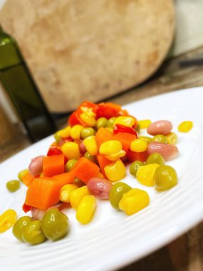 Beyaz tabakta parlak renkli sebzeler: mısır, bezelye, fasulye, biber, havuç, sağlığa iyi gelir, yemek pişirme