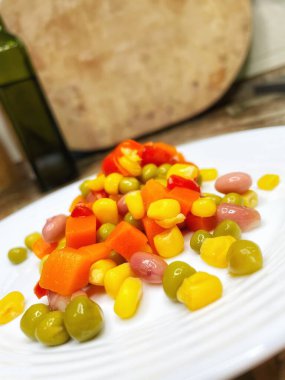 Beyaz tabakta parlak renkli sebzeler: mısır, bezelye, fasulye, biber, havuç, sağlığa iyi gelir, yemek pişirme