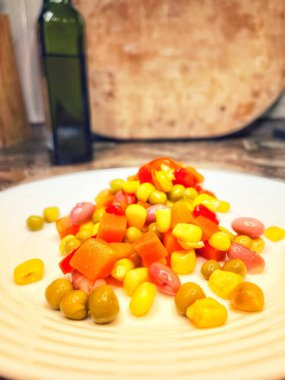 Beyaz tabakta parlak renkli sebzeler: mısır, bezelye, fasulye, biber, havuç, sağlığa iyi gelir, yemek pişirme