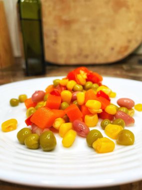 Beyaz tabakta parlak renkli sebzeler: mısır, bezelye, fasulye, biber, havuç, sağlığa iyi gelir, yemek pişirme