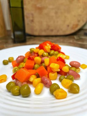 Beyaz tabakta parlak renkli sebzeler: mısır, bezelye, fasulye, biber, havuç, sağlığa iyi gelir, yemek pişirme