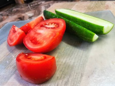 Tahta zemin üzerinde taze organik kırmızı domates ve salatalıklar.