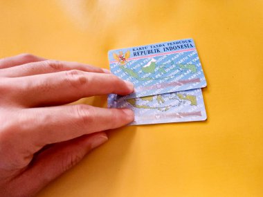 Elinde sarı arkaplan olan iki Endonezya vatandaşı kimlik kartı tutan bir adam. Endonezya kimlik kartının resimli hali. KTP. Makaleler ya da kimlik sorunları için mükemmel.