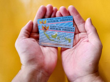 Man hand holding two Indonesian citizen identity card with yellow background. Photo illustration of Indonesia identity card. KTP. perfect for articles, or any identity related issues. clipart