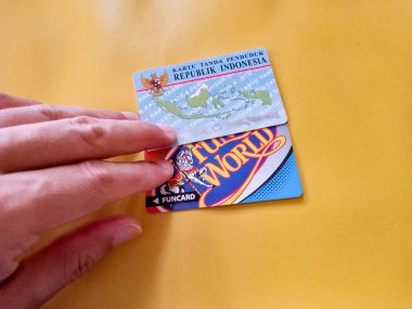 İki Endonezya vatandaşı kimliği ve sarı arka planlı bir zaman kartı. Endonezya kimlik kartı illüstrasyonu. KTP. Makaleler ya da kimlik sorunları için mükemmel.