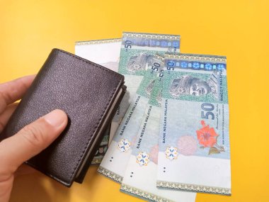 Malezya 50 Ringgit banknotlu cüzdanın sarı arka planda tutulması.