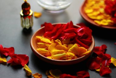 Siyah arka plandaki bir kasede kırmızı ve sarı gül yaprakları. Seçici odak.