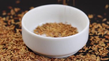 Kimyon tohumları beyaz bir seramik kaseye düşüyor.