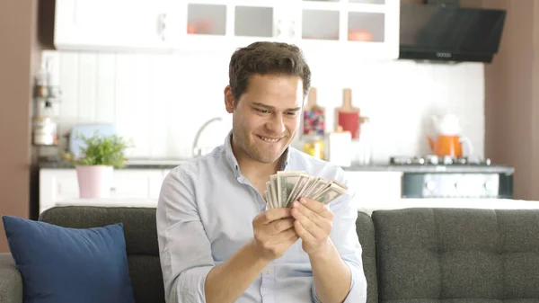 The young man is very happy with his money. Winning the online lottery draw. Happy young male holding many dollars. Excited young man enjoying earning and dollars at home alone.
