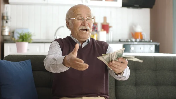 Happy old man excited about his dollars. The old man is sitting on the sofa and counting the banknotes. Portrait of a happy person because he is making a lot of money from betting.