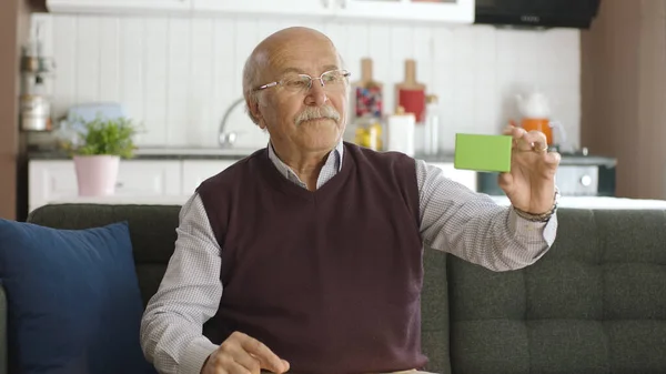 老人正在沙发上看着手中的绿色盒子形状的产品 创意3D艺术家可以用他们想要的任何产品替换绿色盒子 — 图库照片
