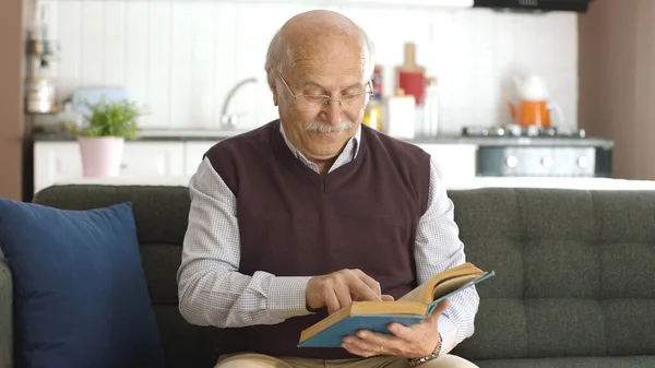 An old man reading a book in his peaceful home enjoying his free time. Happy seniors, retired people concept.
