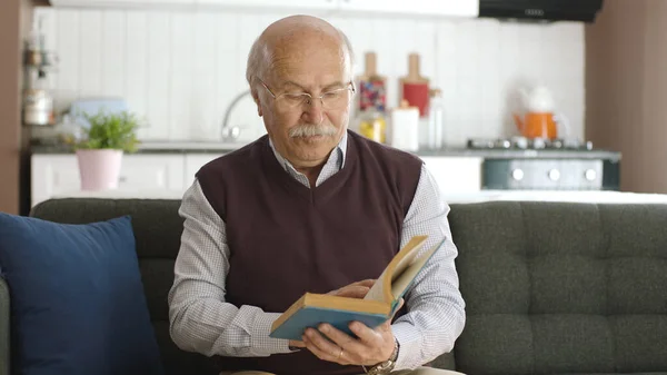 An old man reading a book in his peaceful home enjoying his free time. Happy seniors, retired people concept.