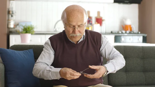 一位老人坐在家中的扶手椅上 用指甲钳剪指甲 个人护理概念 — 图库照片