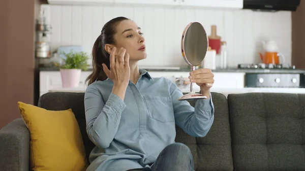 Beautiful happy relaxed woman checking her skin with a small hand mirror. Beauty concept. Skin care. Examining her lips and skin, the young woman is very happy with the view she sees in the mirror.