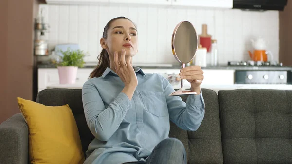 Beautiful happy relaxed woman checking her skin with a small hand mirror. Beauty concept. Skin care. Examining her lips and skin, the young woman is very happy with the view she sees in the mirror.