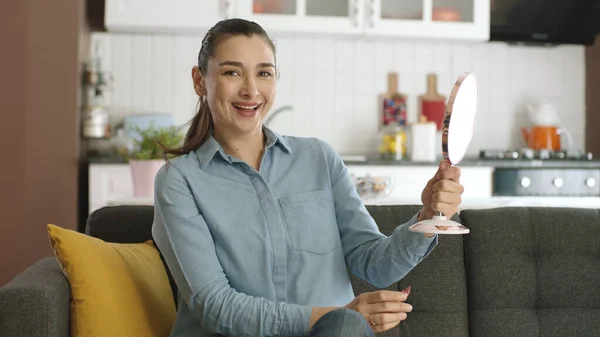 Beautiful happy relaxed woman checking her face with a small hand mirror. Beauty concept. Skin care. The woman is smiling at the camera with a small mirror in her hand.