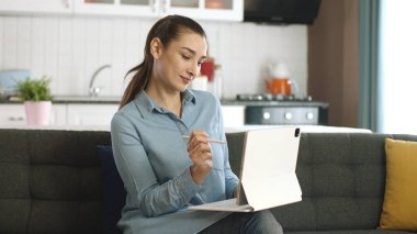 Evdeki kanepede yeni nesil tablet bilgisayarda çalışan genç bir kadın. Yeni teknolojinin kullanımı. Dijital tablet kalem kullanan mutlu serbest çalışan kadın teknoloji cihazıyla çalışıyor..