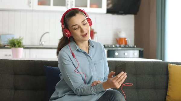 Happy woman dancing to music with headphones connected to her mobile phone in her peaceful home. Woman sitting on sofa using wireless headphones to listen to music at home.