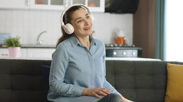 Young happy woman sitting on sofa at home, listening to music with headphones and singing. Home entertainment concept.Happy fun woman portrait.