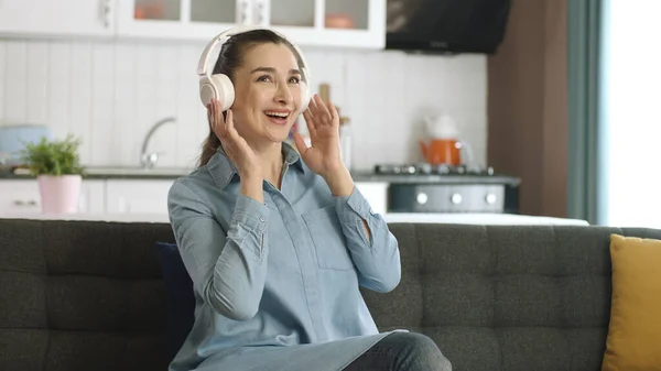 Young happy woman sitting on sofa at home, listening to music with headphones and singing. Home entertainment concept.Happy fun woman portrait.