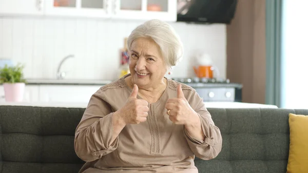 笑着做视频通话的老年妇女 他用大拇指竖起标志向摄像机表明一切都很好 前视镜 — 图库照片