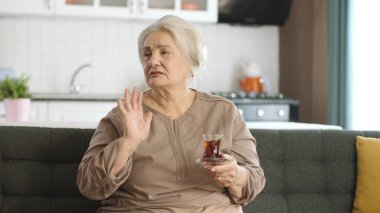 Çay içerken film izleyen mutlu yaşlı kadın ekranın solundaki boş reklam alanına bakıyor. Kanepede tek başına oturup televizyon izleyen yaşlı bir kadın. TV kamerasından görüntü.