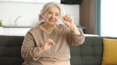 Yaşlı beyaz saçlı bir kadın oturma odasındaki kanepede bir hapı işaret ediyor. Elindeki ilacın mükemmel olduğuna işaret ediyor. Sağlığını, hastalığını, vitaminlerini gösteren mutlu yaşlı kadın..