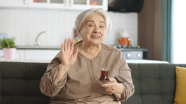 快乐的老妇人一边喝茶一边在电视上看一部有趣的电影 老太太一个人坐在沙发上 看一部神秘的电视电影 老人类 — 图库照片