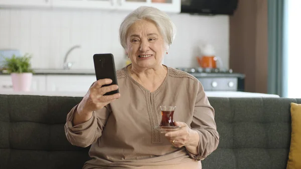 Ευτυχισμένη Γιαγιά Που Κρατάει Κινητό Βιντεοκλήση Αγαπημένους Ενώ Πίνει Τσάι — Φωτογραφία Αρχείου