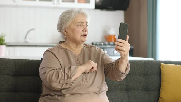 老年妇女与亲戚一起打视频电话 看着相机 坐在舒适的沙发上 老年人的技术使用概念 — 图库照片