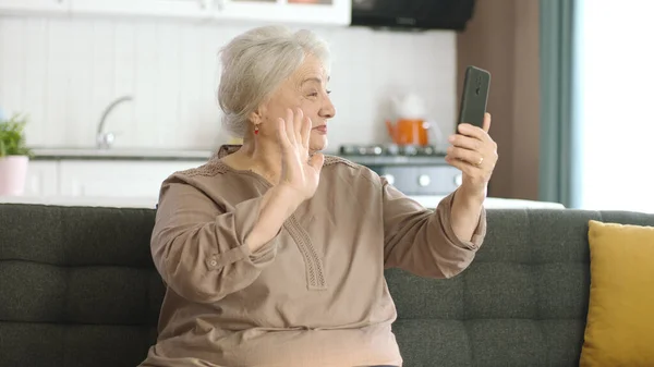 Старшая Женщина Делает Видеозвонок Родственниками Смотрит Камеру Машет Сидит Удобном — стоковое фото